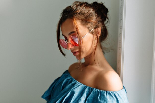 Close-up portret van teder elegant meisje met donker haar en gebruinde huid met stijlvolle jeans top en roze bril