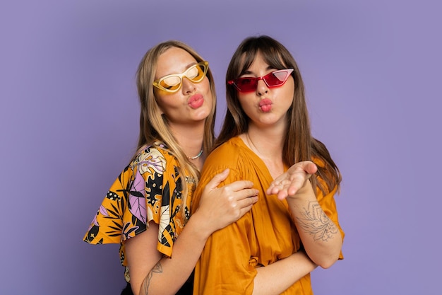 Close-up portret van twee stijlvolle vrouwen in zonnebrillen en trendy zomerkleren poseren op paarse bakground in studio