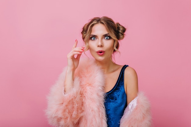 Gratis foto close-up portret van verrast krullend meisje in fluwelen kleding grappig poseren met hand omhoog. geweldige blonde jonge vrouw met trendy make-up herinnerde zich iets belangrijks, geïsoleerd op roze achtergrond.