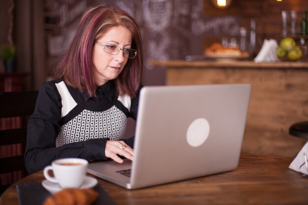 Close-up portret van volwassen zakenvrouw die op laptop werkt en geniet van een kopje koffie in de ochtend
