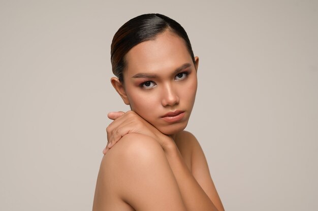 Close-up portret van vrolijke vrouw die zichzelf knuffelt met een charmante glimlach die zich voordeed op een grijze muur in de studio, kijkend naar de camera