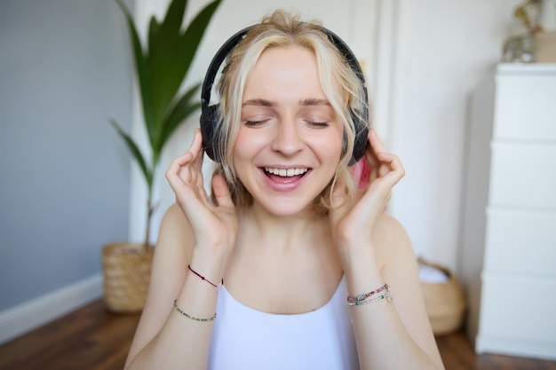 Gratis foto close-up portret van vrouw die glimlacht terwijl ze naar muziek luistert in draadloze koptelefoon die met ogen zingt