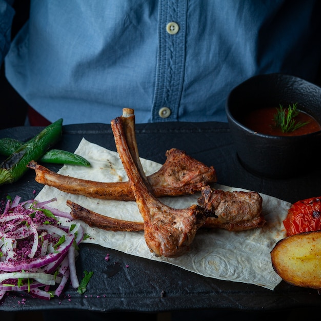 Gratis foto close-up ribs gegrilde ribbetjes op pitabroodje met gebakken aardappelen, paprika, tomaat, gehakte ui en saus