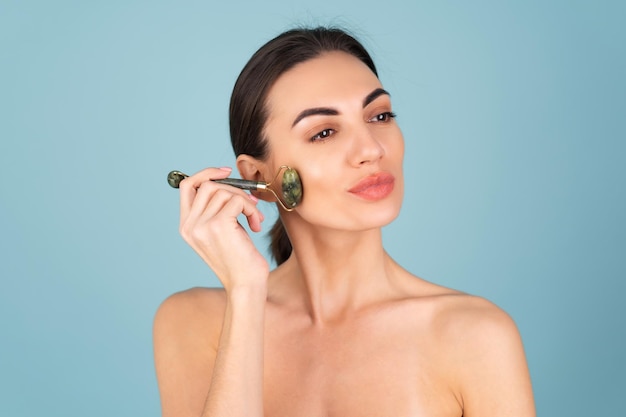 Close-up schoonheidsportret van een vrouw met perfecte huid en natuurlijke make-up, mollige naakte lippen, met een roller stimulator voor gezicht en nek
