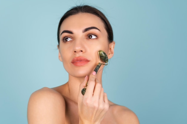 Close-up schoonheidsportret van een vrouw met perfecte huid en natuurlijke make-up, mollige naakte lippen, met een roller stimulator voor gezicht en nek