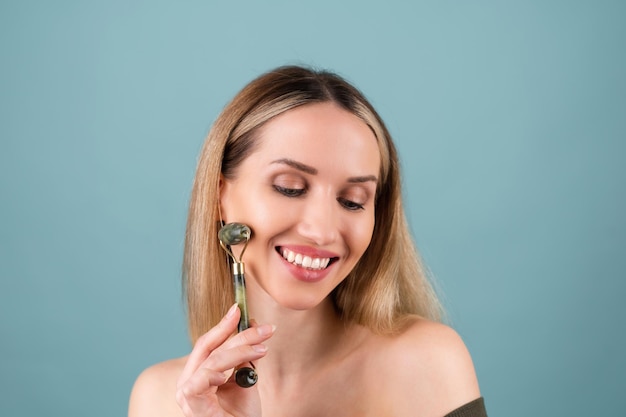 Close-up schoonheidsportret van een vrouw met perfecte huid en natuurlijke make-up, mollige naakte lippen, met een roller stimulator voor gezicht en nek