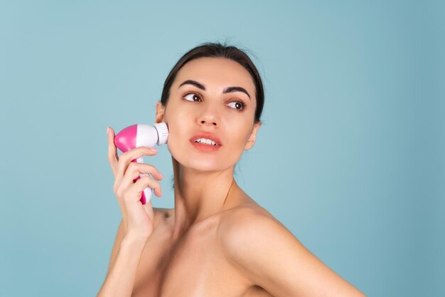 Close-up schoonheidsportret van topless vrouw met perfecte huid en natuurlijke make-up, volledige naakte lippen, met een elektrische gezichtsborstel. Gezichtsreiniging met microvibraties