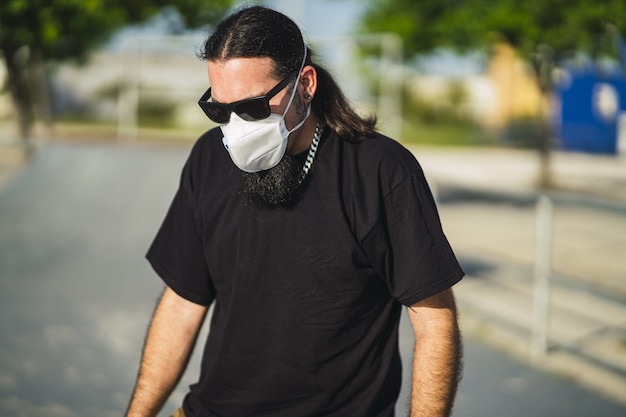 Close-up shot van een bebaarde man in een zwart shirt met een medisch gezichtsmasker in het park