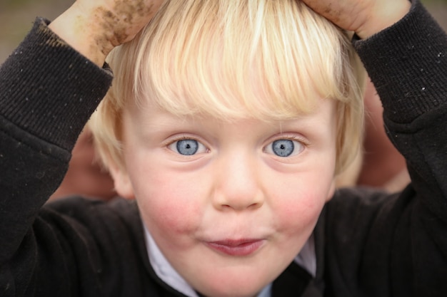 Close-up shot van een blanke blanke jongen met blauwe ogen die zijn hoofd vasthoudt met modderige handen