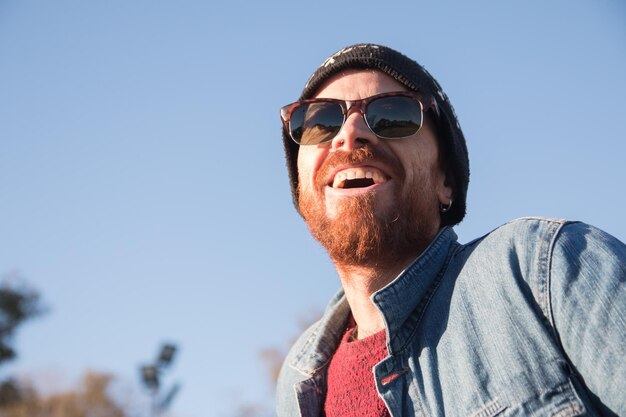 Close-up shot van een blanke knappe man met baard en zonnebril lachend onder de zon