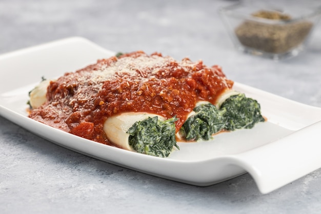 Close-up shot van een Cannelloni gerecht gevuld met spinazie en ricotta geserveerd met bolognese saus