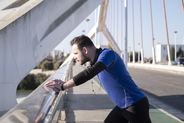 Close-up shot van een jonge man leunend op de rand van de brug tijdens het joggen