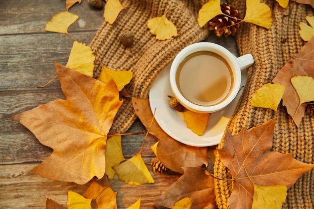 Close-up shot van een kopje koffie en herfstbladeren op houten oppervlak