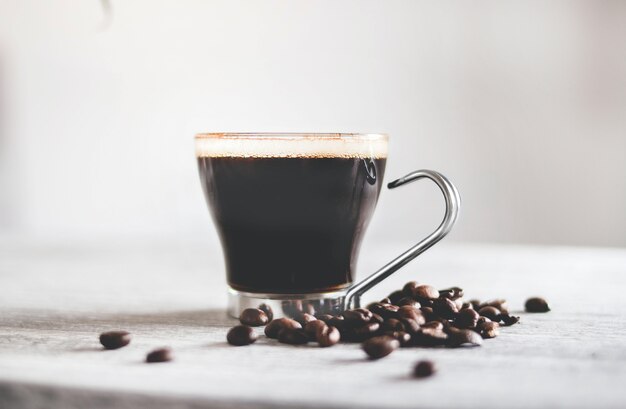 Close-up shot van een kopje zwarte koffie op tafel met geroosterde bonen onder de lichten