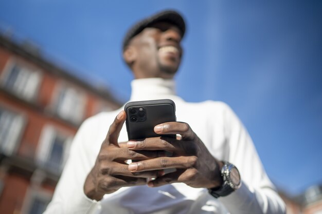 Close-up shot van een man met een coltrui en een hoed die zijn telefoon vasthoudt