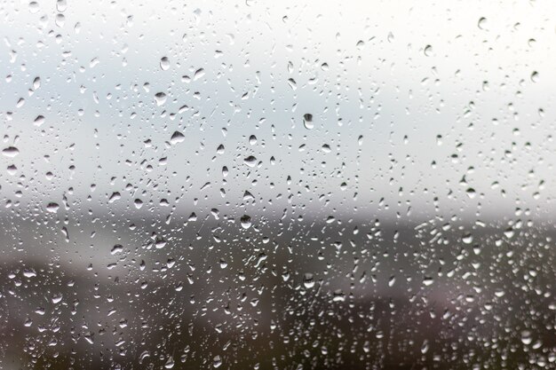 Close-up shot van een raam op een regenachtige dag, regendruppels die door het raam rollen