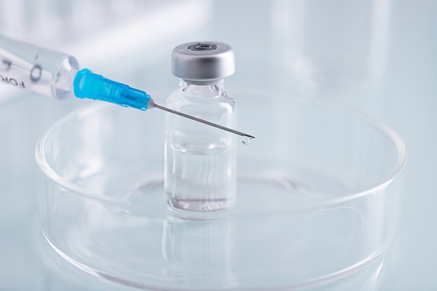 Close-up shot van een spuit en een open glazen injectieflacon met heldere vloeistof in een glazen schaal in een lab