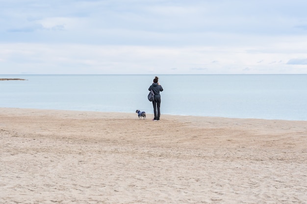 Close-up shot van een vrouw met haar hond die op een strand staat en het prachtige uitzicht observeert