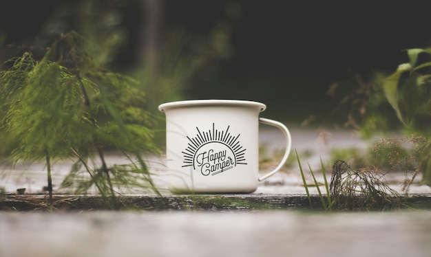 Close-up shot van een wit metalen beker met "Happy Camper" schrijven op een houten oppervlak in de buurt van groene planten