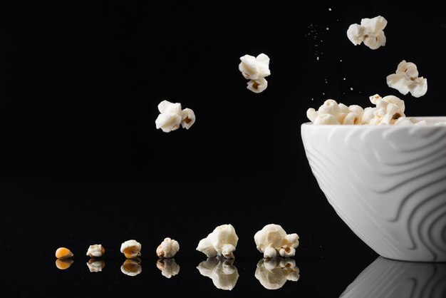 Close-up shot van een witte kom met knallende pop-corn uit op een donkere achtergrond