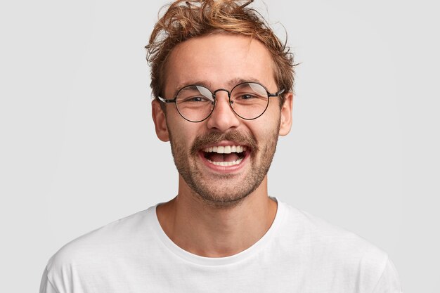 Close-up shot van gelukkig stijlvolle man in ronde bril, heeft een positieve glimlach op het gezicht, blij om salaris te ontvangen, gaat geld uitgeven aan nieuwe aankopen