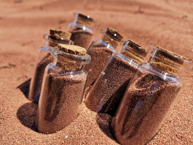 Gratis foto close-up shot van glazen potten gevuld met rood zand in het zand op het strand