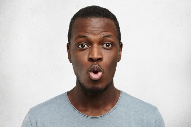Close-up shot van grappige jonge African American man gekleed terloops lippen pruilen en wenkbrauwen verhogen