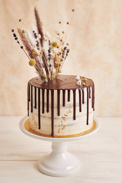 Close-up shot van heerlijke Boho-cake met chocoladedruppel en bloemen bovenop met gouden versieringen
