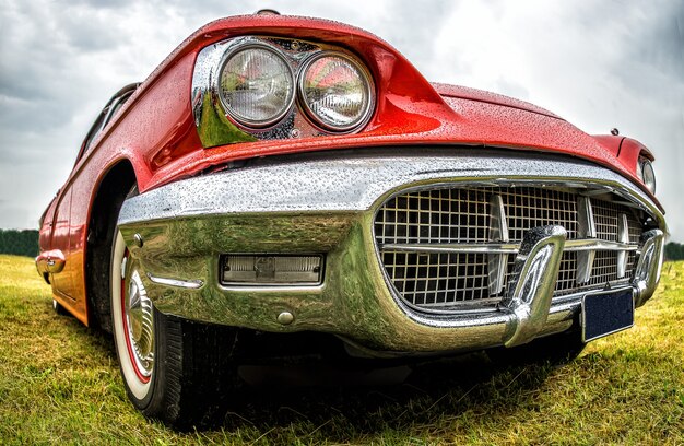 Close-up shot van het voorste deel van een rode auto geparkeerd op een groen veld