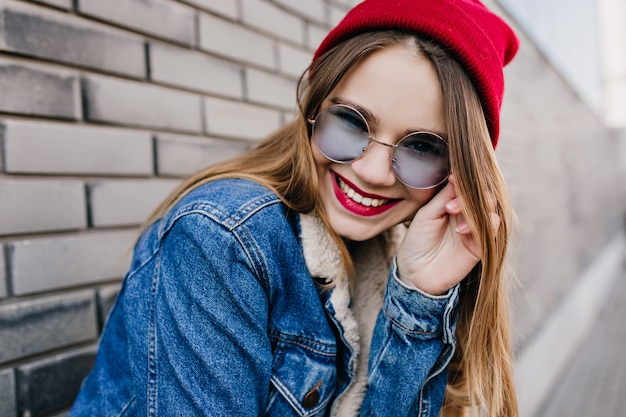 Close-up shot van Kaukasisch fascinerend meisje in casual rode jurk. Foto van enthousiaste blanke vrouw draagt denim kleding in de lente.