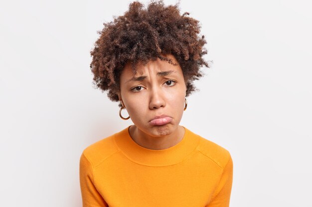 Close-up shot van ontevredenheid trieste Afro-Amerikaanse vrouw ontevreden beledigd door iemand gekleed in oranje trui geïsoleerd over witte muur voelt spijt en verdriet. Negatieve emoties