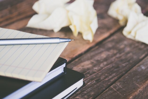 Close-up shot van schoolboeken met een grijze pen en verfrommelde stukjes papier rond op een houten oppervlak