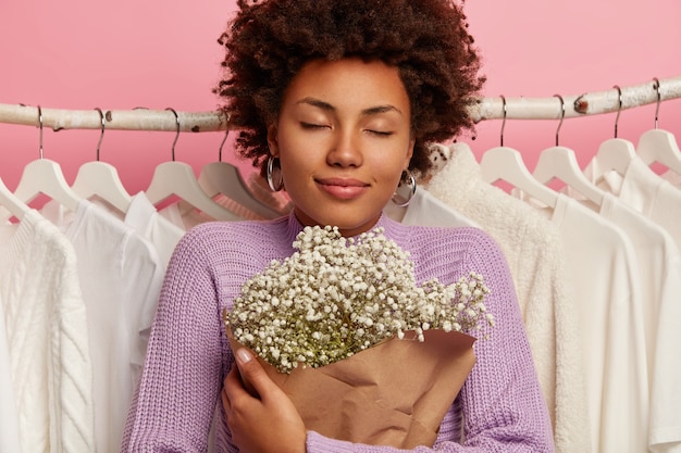 Close-up shot van tevreden vrouw houdt mooi boeket, houdt de ogen gesloten geniet van aangename geur, poses tegen kleren opknoping in kledingkast op rekken