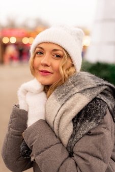 Close-up straat portret van lachende mooie jonge vrouw op de feestelijke kerstmarkt. dame die klassieke stijlvolle winter gebreide kleding draagt.