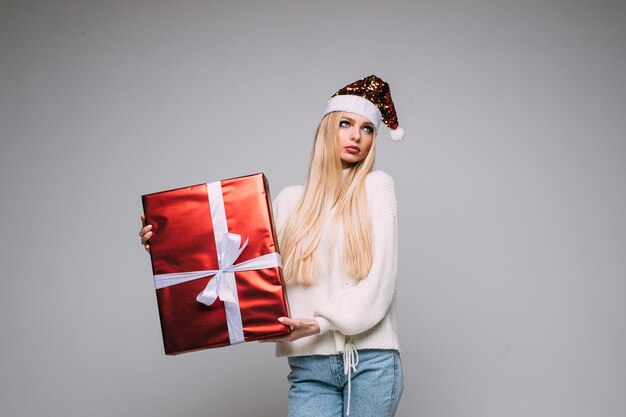 Close-up studiofoto van een mooie jonge dame in kerstmuts die handen rond de mond houdt en gezichten trekt