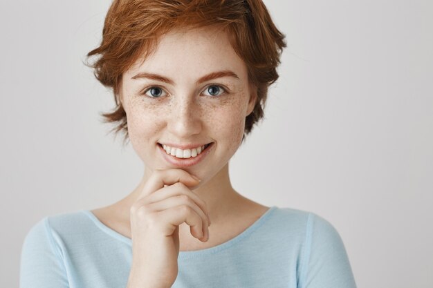Close-up van aantrekkelijk en roodharig meisje dat verleidelijk glimlacht kijkt