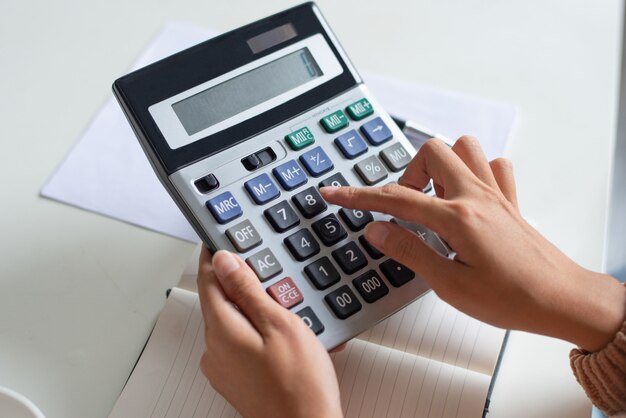 Close-up van accountant die calculator gebruikt terwijl het onderzoeken van rapport