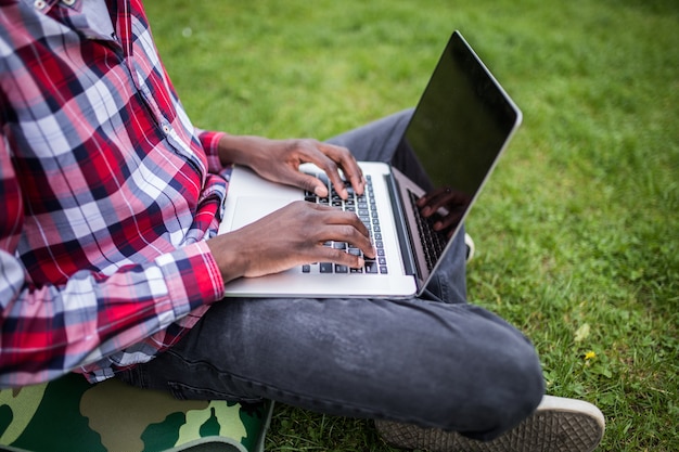Close-up van afro Amerikaanse handen typen op laptop op groen gras