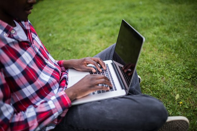 Close-up van afro Amerikaanse handen typen op laptop op groen gras