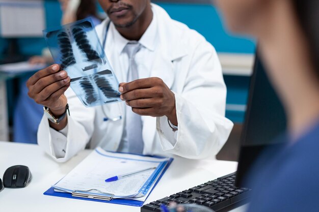 Close-up van Afro-Amerikaanse kinderarts arts die longen radiografie vasthoudt en röntgenexpertise uitlegt aan geduldige moeder die medische behandeling in het ziekenhuiskantoor bespreekt. Gezondheidszorg