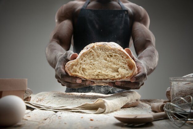 Close up van Afro-Amerikaanse man kookt vers ontbijtgranen, brood, zemelen op houten tafel. Lekker eten, voeding, ambachtelijk product. Glutenvrij eten, gezonde levensstijl, biologisch en veilig geproduceerd. Handgemaakt.