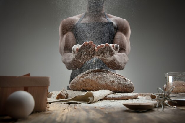 Close up van Afro-Amerikaanse man kookt vers ontbijtgranen, brood, zemelen op houten tafel. Lekker eten, voeding, ambachtelijk product. Glutenvrij eten, gezonde levensstijl, biologisch en veilig geproduceerd. Handgemaakt.