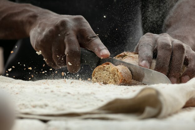 Close up van Afro-Amerikaanse man snijdt vers brood met een keukenmes