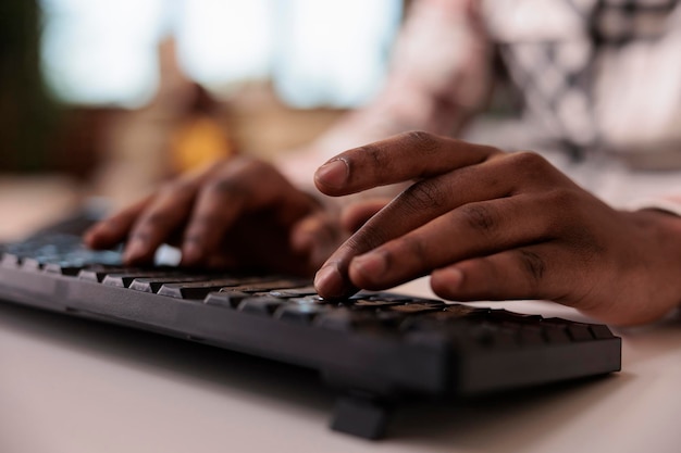 Gratis foto close-up van afro-amerikaanse mannelijke inhoudsmaker die post schrijft voor sociale media op computertoetsenbord in de huiskamer. selectieve focus op man handen werken op afstand blogartikel typen.