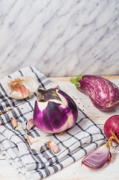 Gratis foto close-up van aubergines; ui; knoflookteentjes en geruit patroon textiel op houten oppervlak
