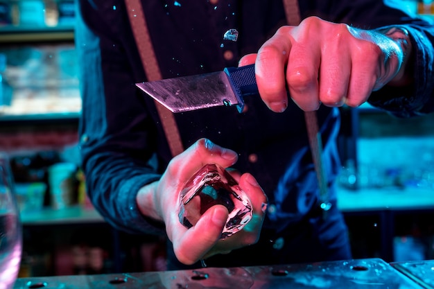 Close-up van barman die een groot stuk ijs op de toog verplettert met een speciale baruitrusting erop voor een cocktail