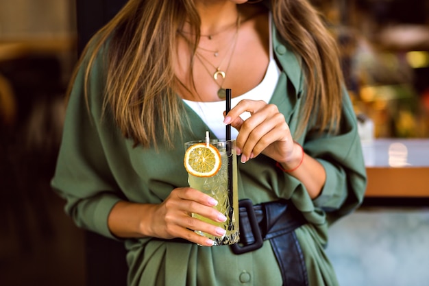 Close-up van bijgesneden afbeelding van vrouw met zoete smakelijke cocktail limonade, stijlvolle trendy hipster outfit en elegante sieraden, afgezwakt kleuren, sfeer van de bar.