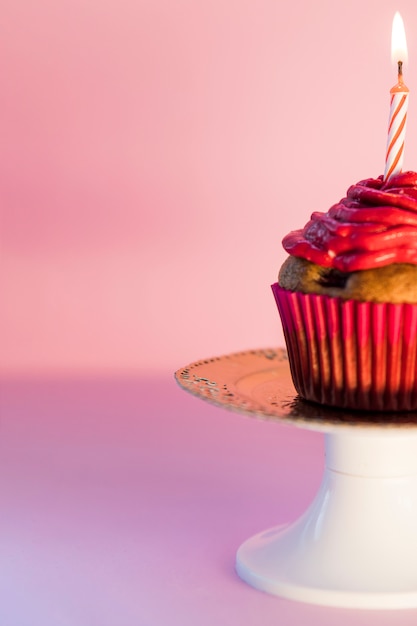 Close-up van brandende kaars over de cupcake op cakestand tegen roze achtergrond