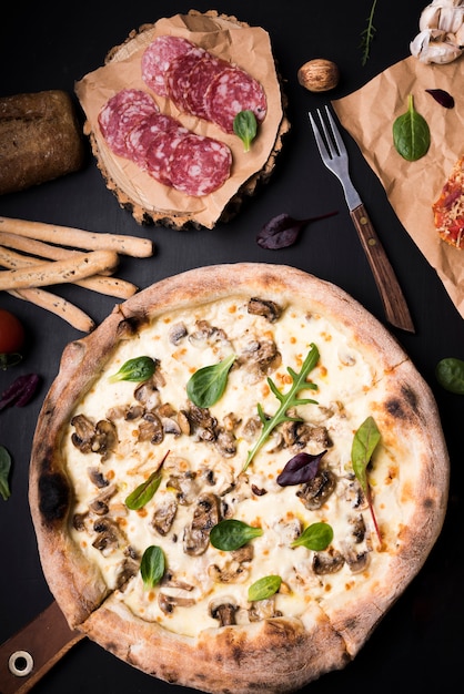 Close-up van champignonkaaspizza; plakjes pepperoni; broodstokken en vork op de balie