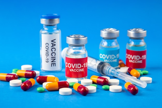 Close-up van COVID-vaccins in medische ampullen pillen capsules wegwerpspuit op donkere en zachte blauwe achtergrond